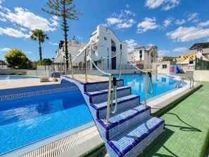 A swimming pool with blue-tiled steps and a white building in the background. - Charming Upper Bungalow with Terrace and Communal Pool in Torrevieja (Torrevieja)