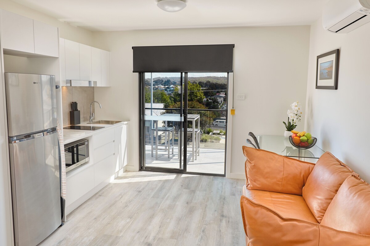 A modern kitchen with a stainless steel refrigerator, white cabinets, and a sliding glass door leading to an outdoor area with a table and chairs.