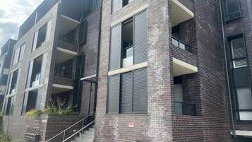 A multi-story building with a brick facade, balconies, and a staircase leading to the entrance.