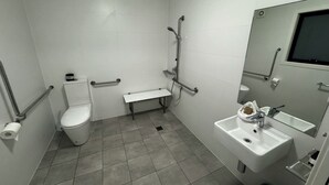 Ein Badezimmer mit Toilette, Sitzbank, Waschbecken und Dusche.