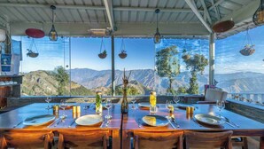 Un espace repas avec des tables disposées pour accueillir quatre personnes, offrant une vue sur un paysage montagneux.
