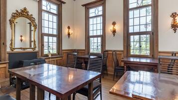 A dining area with wooden tables and chairs, large windows, and a decorative mirror.