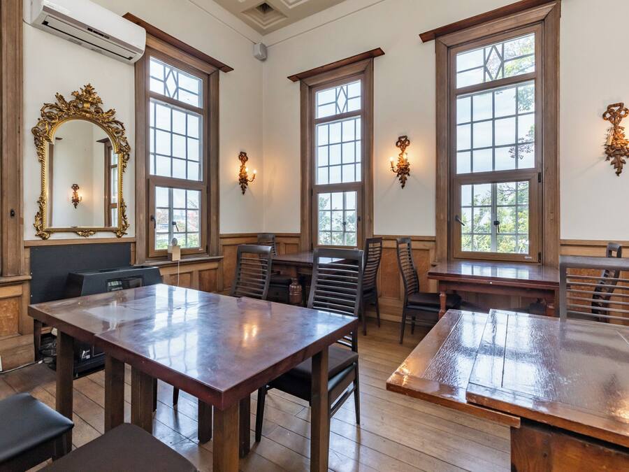 A dining area with wooden tables and chairs, large windows, and a decorative mirror.