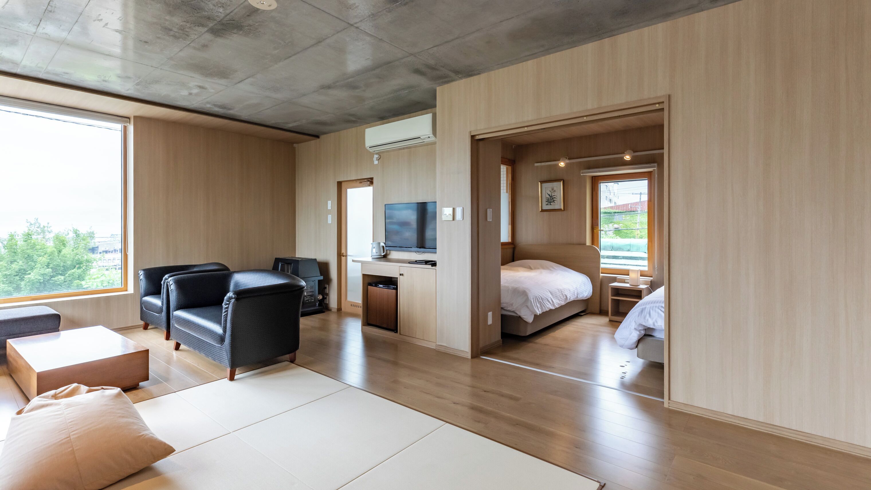 A modern hotel room with a sofa, a TV, a bed, and a view of the outdoors.