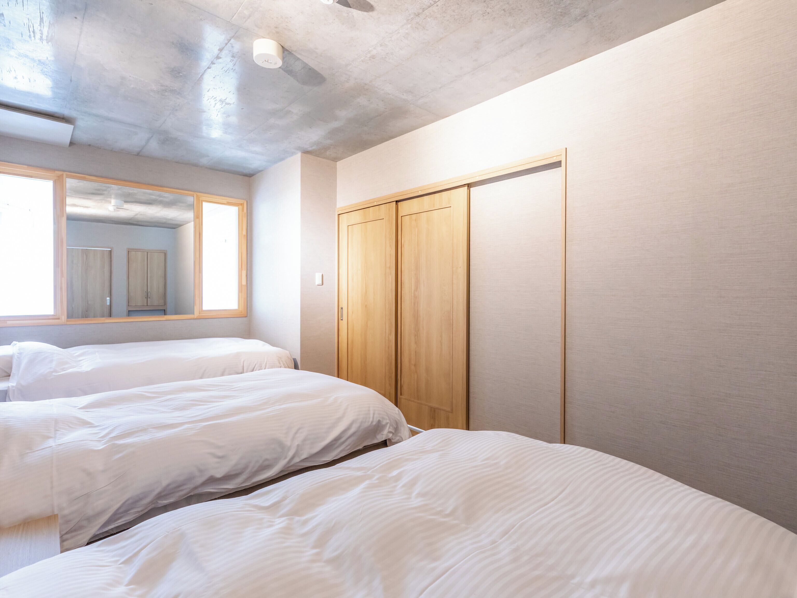 A bedroom with two beds, a wooden wardrobe, and a large window.
