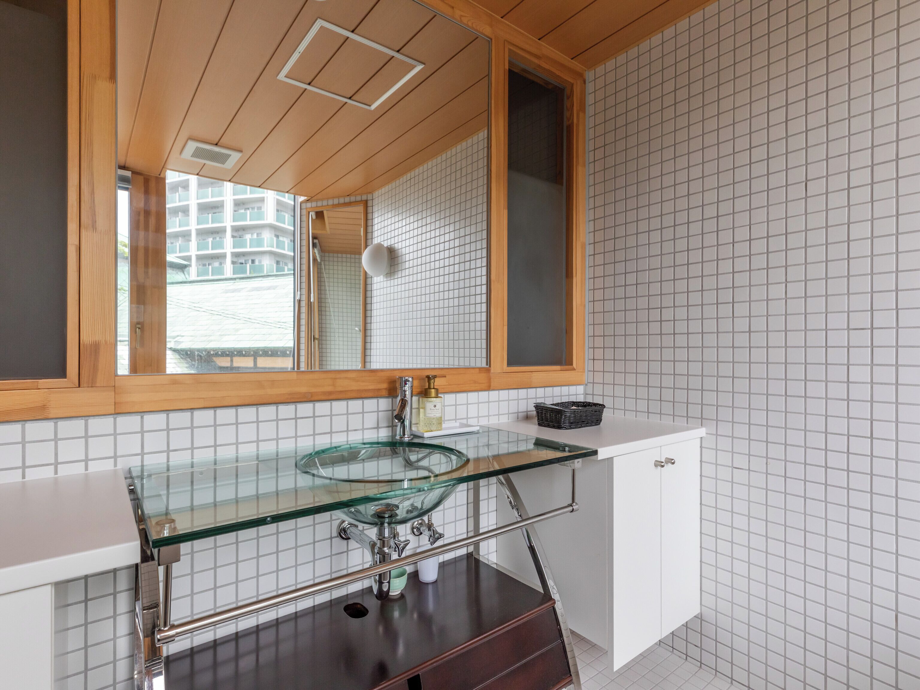 Een moderne badkamer met een glazen wastafel, houten plafond en betegelde wanden.