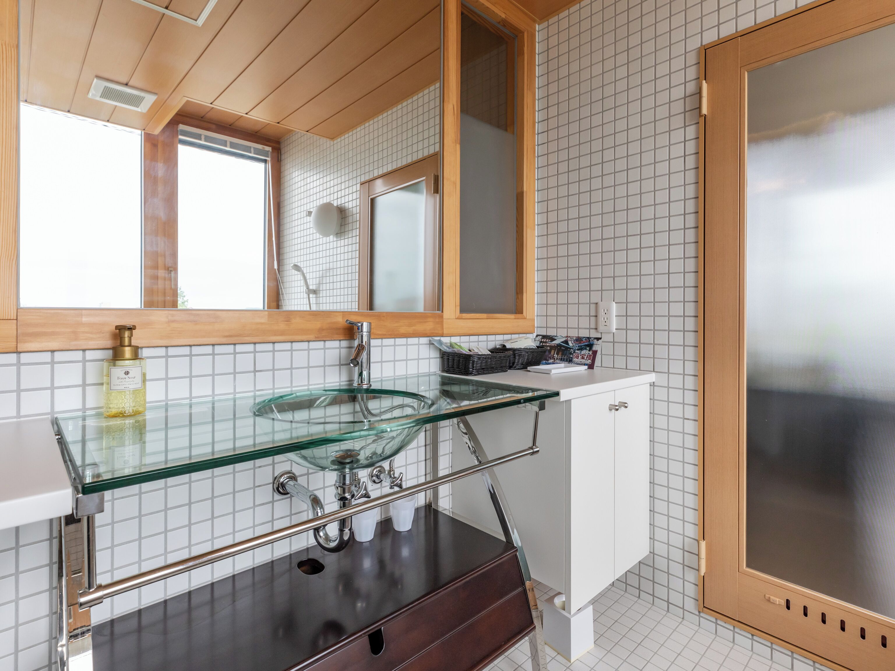 A modern bathroom with a glass sink, wooden vanity, and a large mirror.