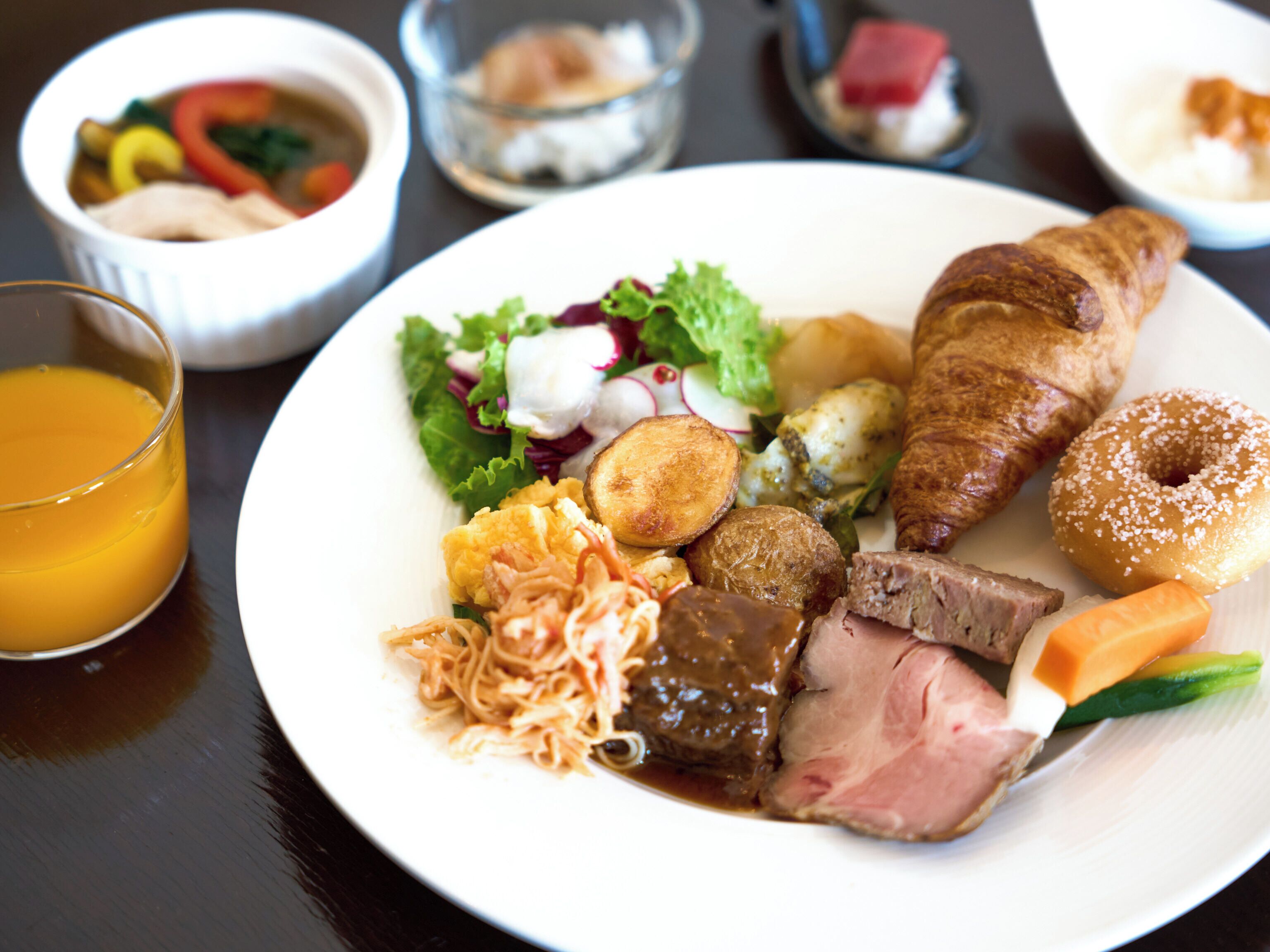 A plate of food including meat, vegetables, and a croissant.