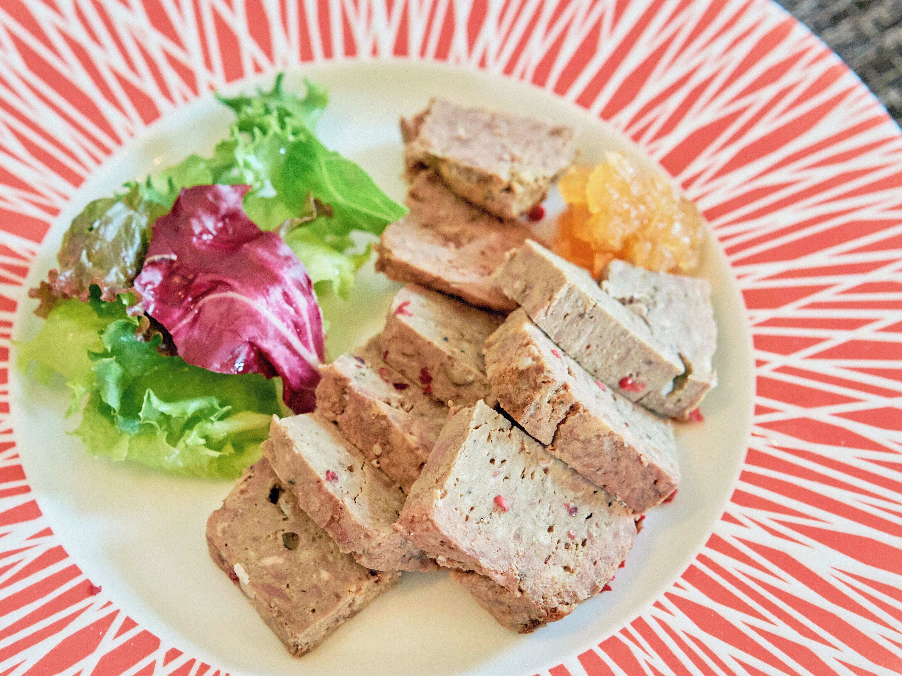 Une assiette contenant de la viande en tranches, des légumes et un fruit.