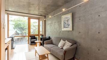 A modern living room with a sofa, chairs, a small table, and a large window offering a view of a traditional building and trees.
