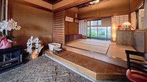 Ein traditioneller japanischer Raum mit Tatami-Böden, einem niedrigen Holztisch, einer schwarzen Mikrowelle und einem kleinen weißen Tisch mit einer Vase weißer Orchideen.