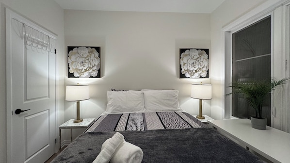 A bedroom with a bed, two bedside lamps, a window, and a door.
