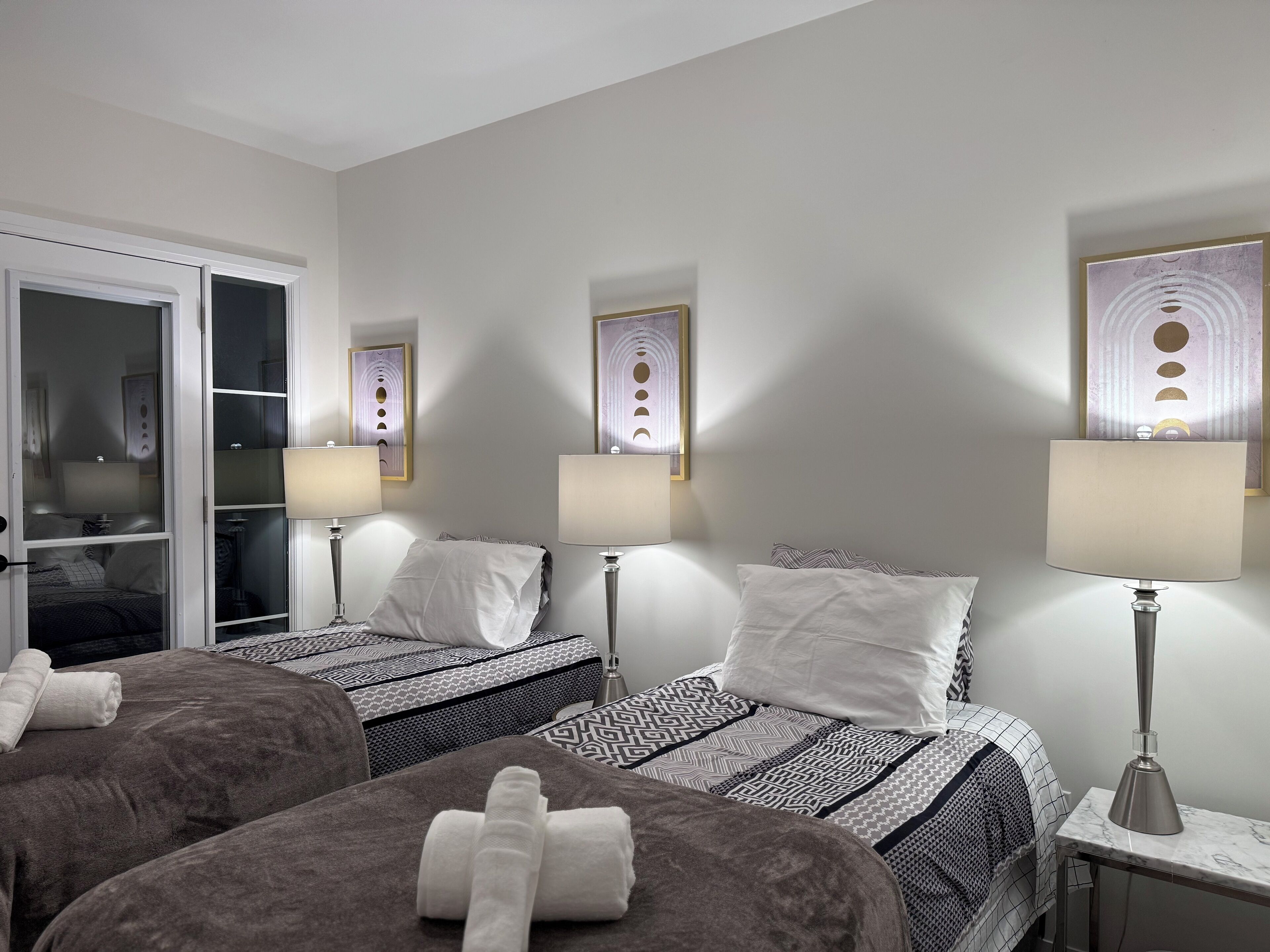 Habitación de hotel con dos camas, cada una con ropa de cama estampada y almohadas blancas. Hay dos lámparas de noche y un espejo en la pared.