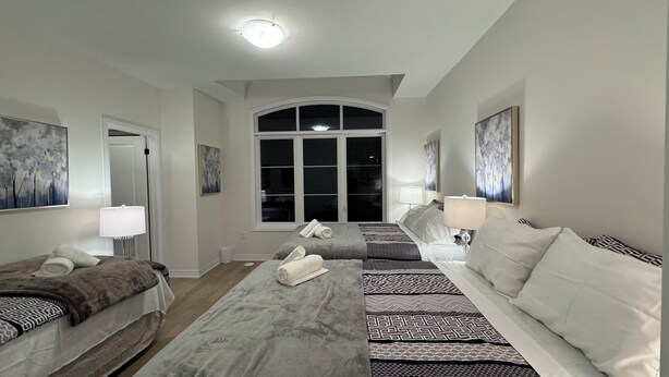 A hotel room with a large arched window, two beds with patterned bedding, a central seating area, and artwork on the walls. - Elegant Townhome in Prestigious Woodbridge Estate, Vaughan (Selena) (Vaughan)