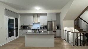 A modern kitchen with white cabinets, a stainless steel refrigerator, and a central island with a sink. - Elegant Townhome in Prestigious Woodbridge Estate, Vaughan (Selena) (Vaughan)