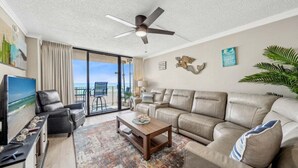 Een woonkamer met een bank, salontafel, televisie en een balkon met uitzicht.