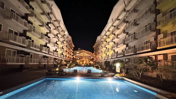 A nighttime view of a hotel with a central swimming pool, surrounded by multi-story buildings with balconies.