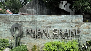 A sign for 'AMANT GRAND RESORT RESIDENCES' with a stone wall and greenery around it.