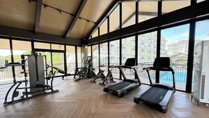 A gym with exercise equipment, large windows, and a herringbone floor pattern.