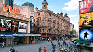 Een levendig stadsplein met historische architectuur, een Vue bioscoop en een Genuis espressobar.