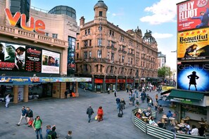 Una plaza urbana concurrida con arquitectura histórica, un cine Vue y una cafetería Genuis de espresso.