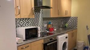Een kleine keuken met houten kastjes, een magnetron, een oven en een wasmachine.