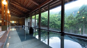 Um espaço amplo e interno, com piso de vidro, grandes janelas com vista para uma paisagem arborizada e vigas de madeira no teto.