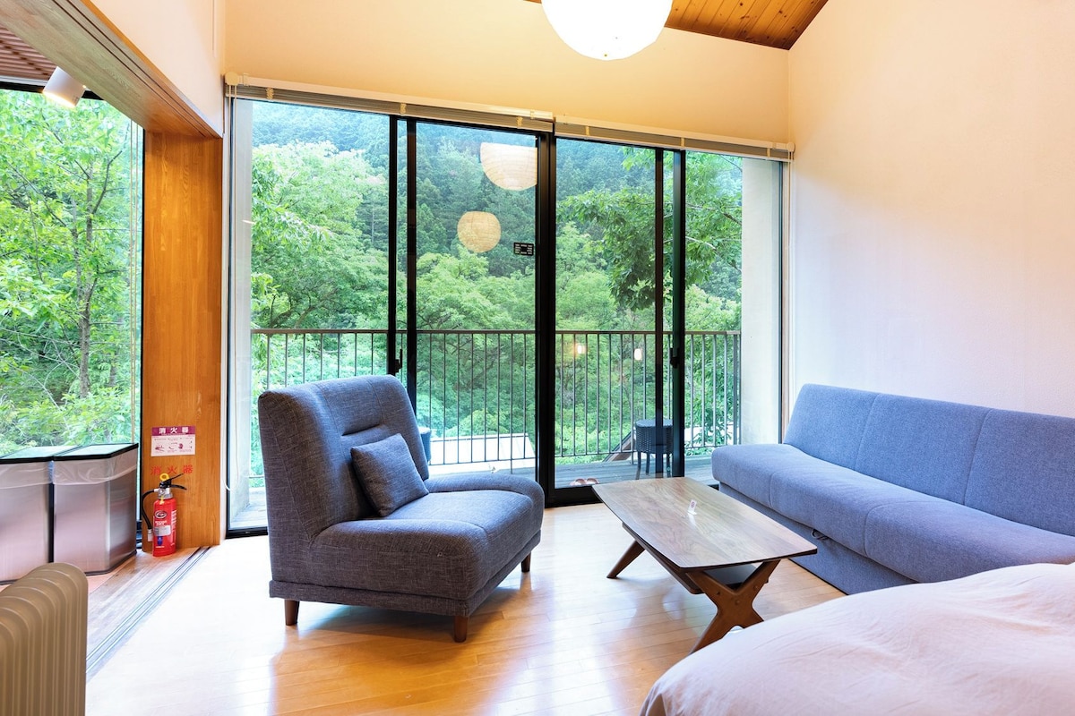 A modern room with a large sliding glass door leading to a balcony, a grey armchair, a blue sofa, and a wooden coffee table.