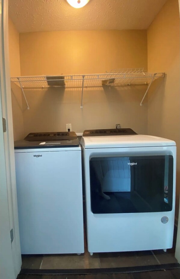 A laundry room with a Whirlpool washer and dryer, a metal drying rack, and a light fixture on the ceiling.