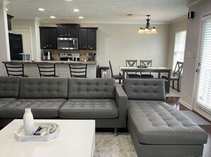 A modern living room with a sectional sofa, a coffee table, and a dining area with a table and chairs.