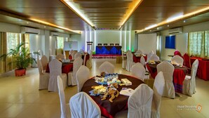 A conference room with round tables, white chairs, and a stage with a blue curtain. - Hotel Beach Way (Cox's Bazar)