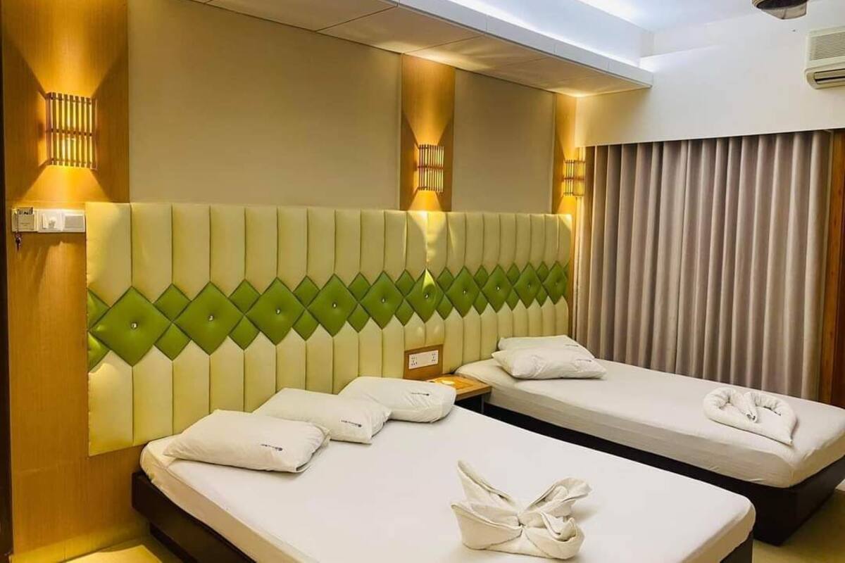 A hotel room with two beds, a headboard with a diamond pattern, wall-mounted lights, and a ceiling fan.