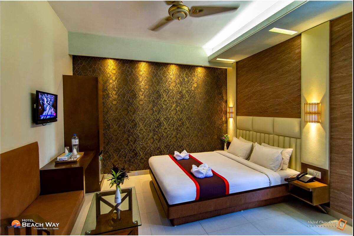 A hotel room with a bed, bedside table, lamp, and a television on the wall.