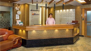 A hotel reception desk with a receptionist, a clock, framed certificates, and a sign that reads "Hotel Beach Way". - Hotel Beach Way (Cox's Bazar)