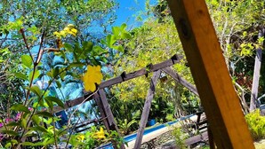 A wooden swing set in a garden with a pool in the background. - Rancho Fernandez (Jarabacoa)