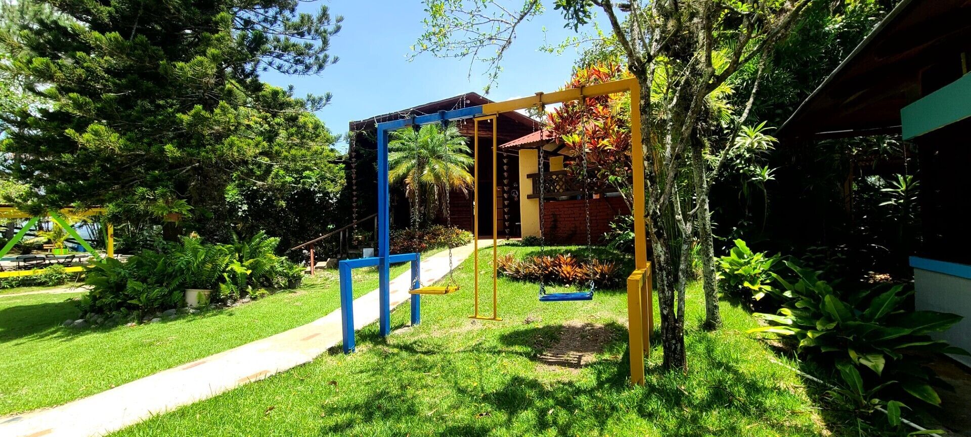 A playground with swings and a slide, surrounded by greenery and a building.