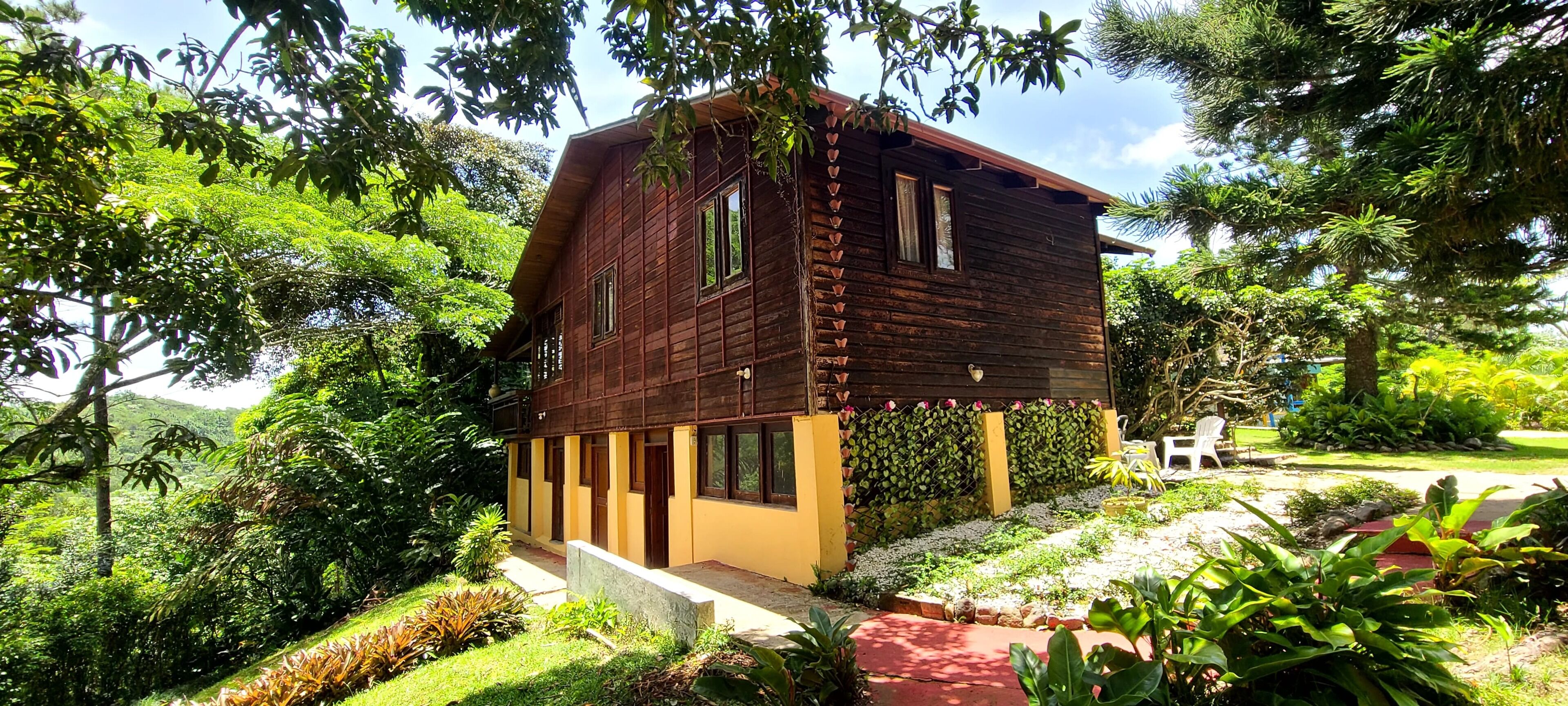 Una casa de madera con balcón, rodeada de exuberante vegetación y un jardín bien cuidado.