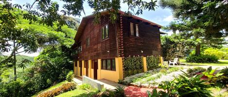 Una casa de madera con balcón, rodeada de exuberante vegetación y un jardín bien cuidado.