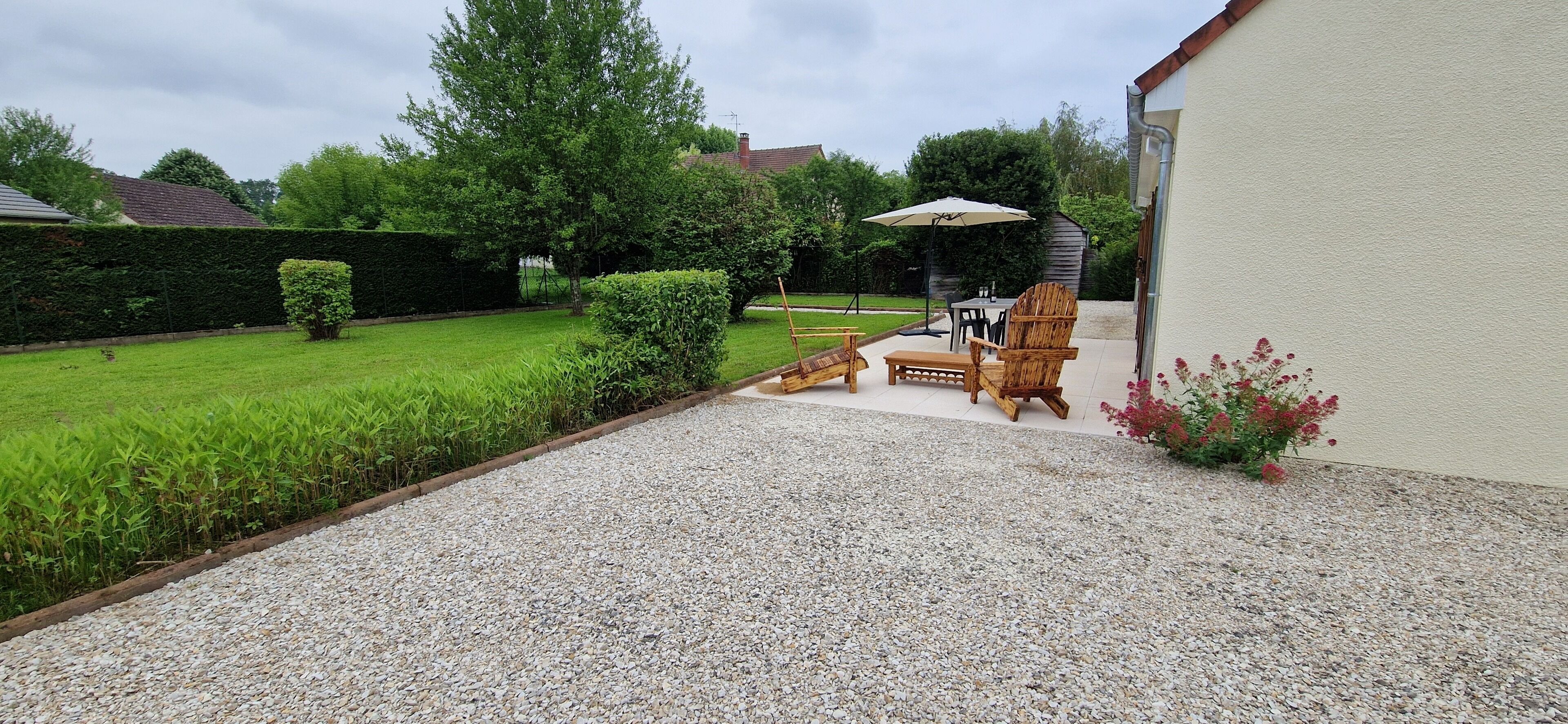 Een achtertuin met een terras, een houten stoel, een tafel en een parasol.