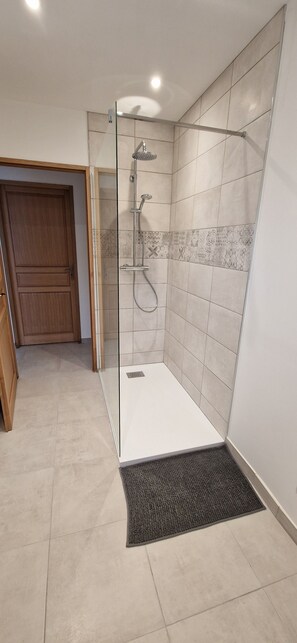 A modern shower area with a glass door, tiled walls, and a wooden door in the background. - Au Jardin D'olga (Mesnil-Saint-Père)
