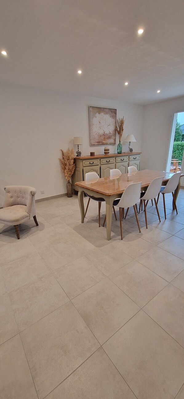 A dining area with a wooden table and chairs, a vase with dried plants, and a painting on the wall. - Au Jardin D'olga (Mesnil-Saint-Père)