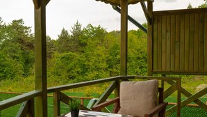 Eine Holzterrasse mit Tisch und Stühlen, einem Blumentopf und Blick auf Grünflächen.