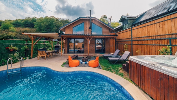 Ein Garten mit Swimmingpool, Holzterrasse, Whirlpool und Sitzgelegenheit im Freien.