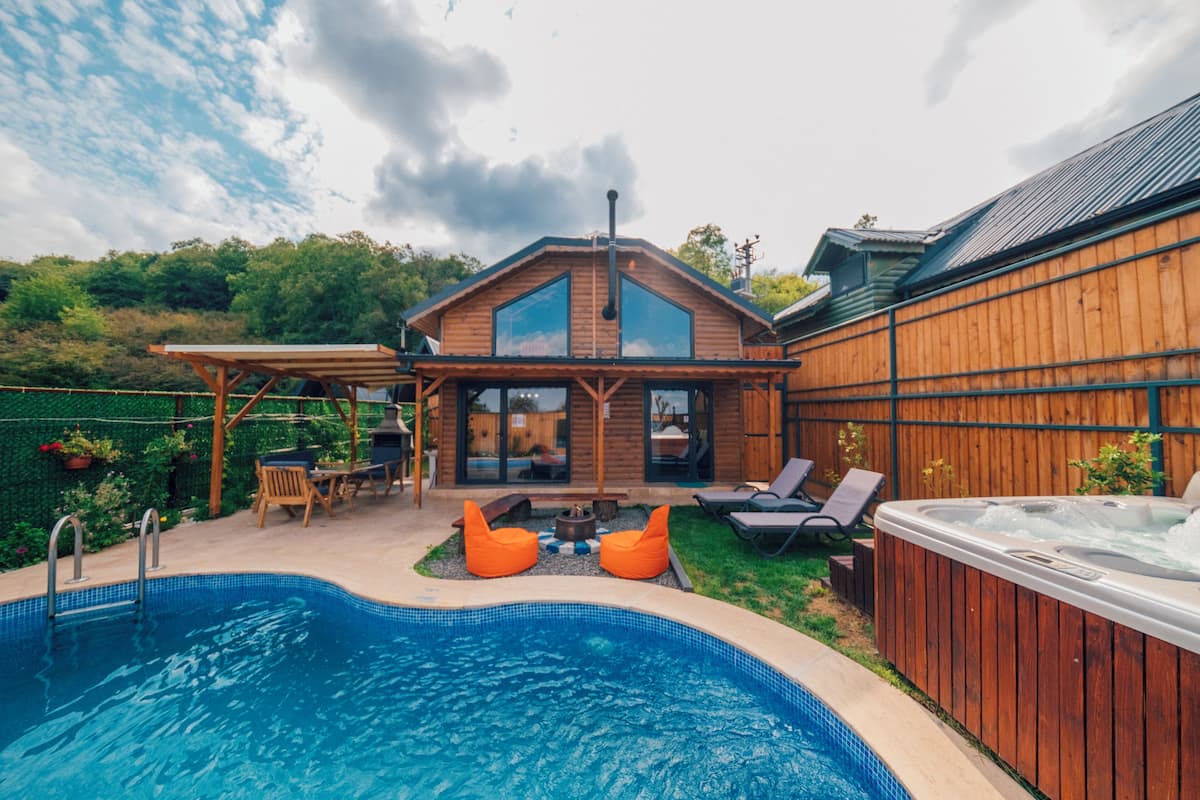 A backyard with a swimming pool, wooden deck, hot tub, and outdoor seating area.