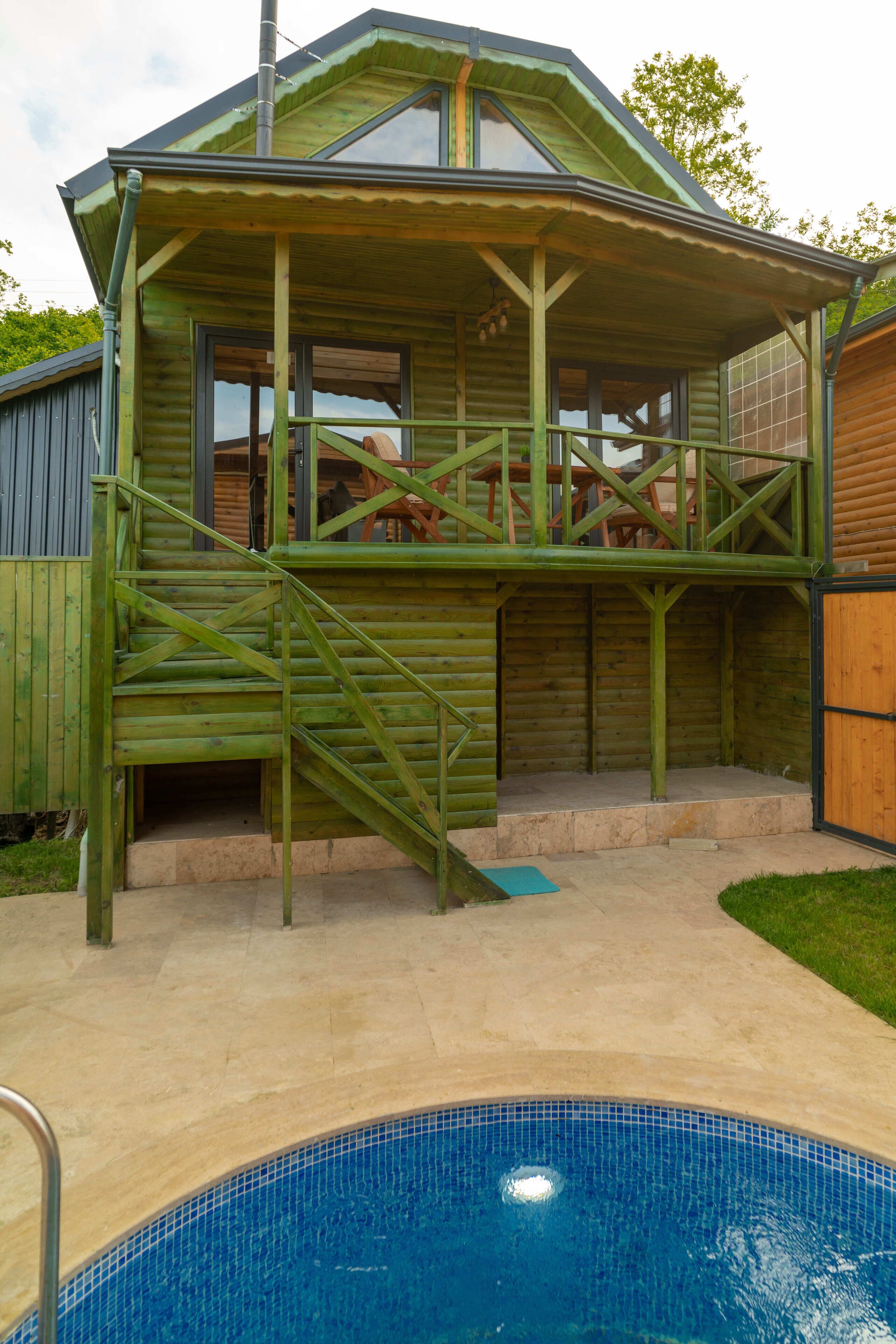 A wooden cabin with a balcony, a pool, and a staircase leading to the entrance.