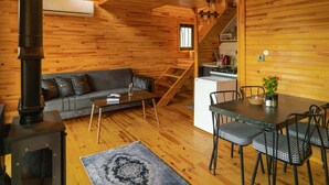 Ein gemütliches Blockhaus-Interieur mit einer Couch, einem Esstisch, Stühlen, einem Kamin und einer Küchenzeile.