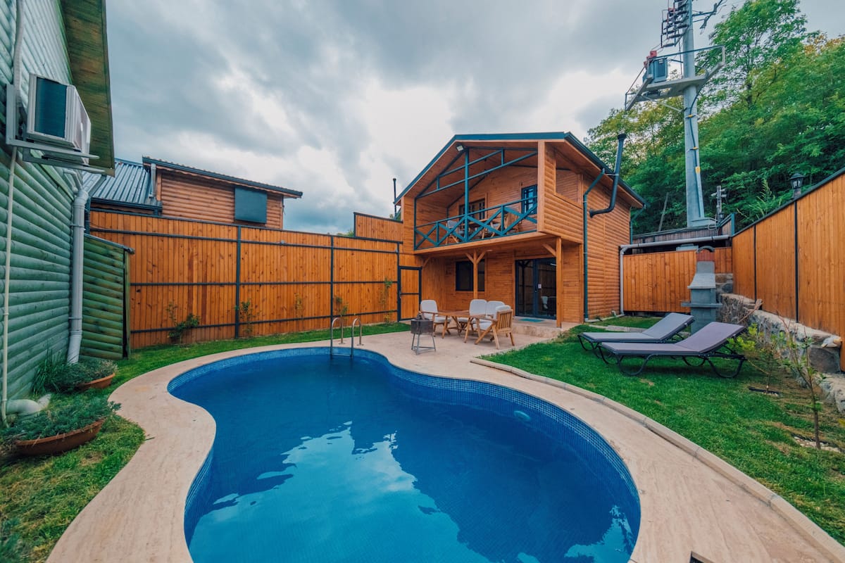 A backyard with a swimming pool, wooden fence, and a two-story wooden house with a balcony.