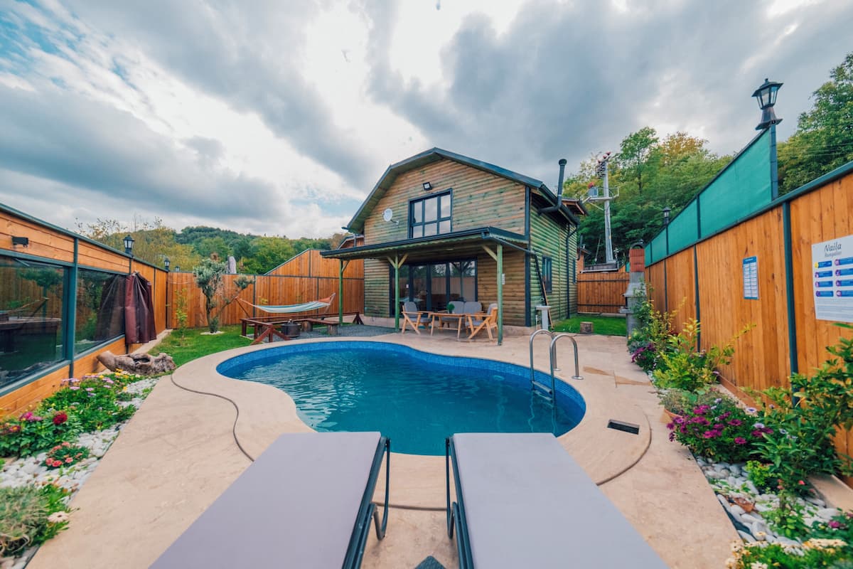 A backyard with a swimming pool, wooden deck, and a small wooden house with outdoor furniture.