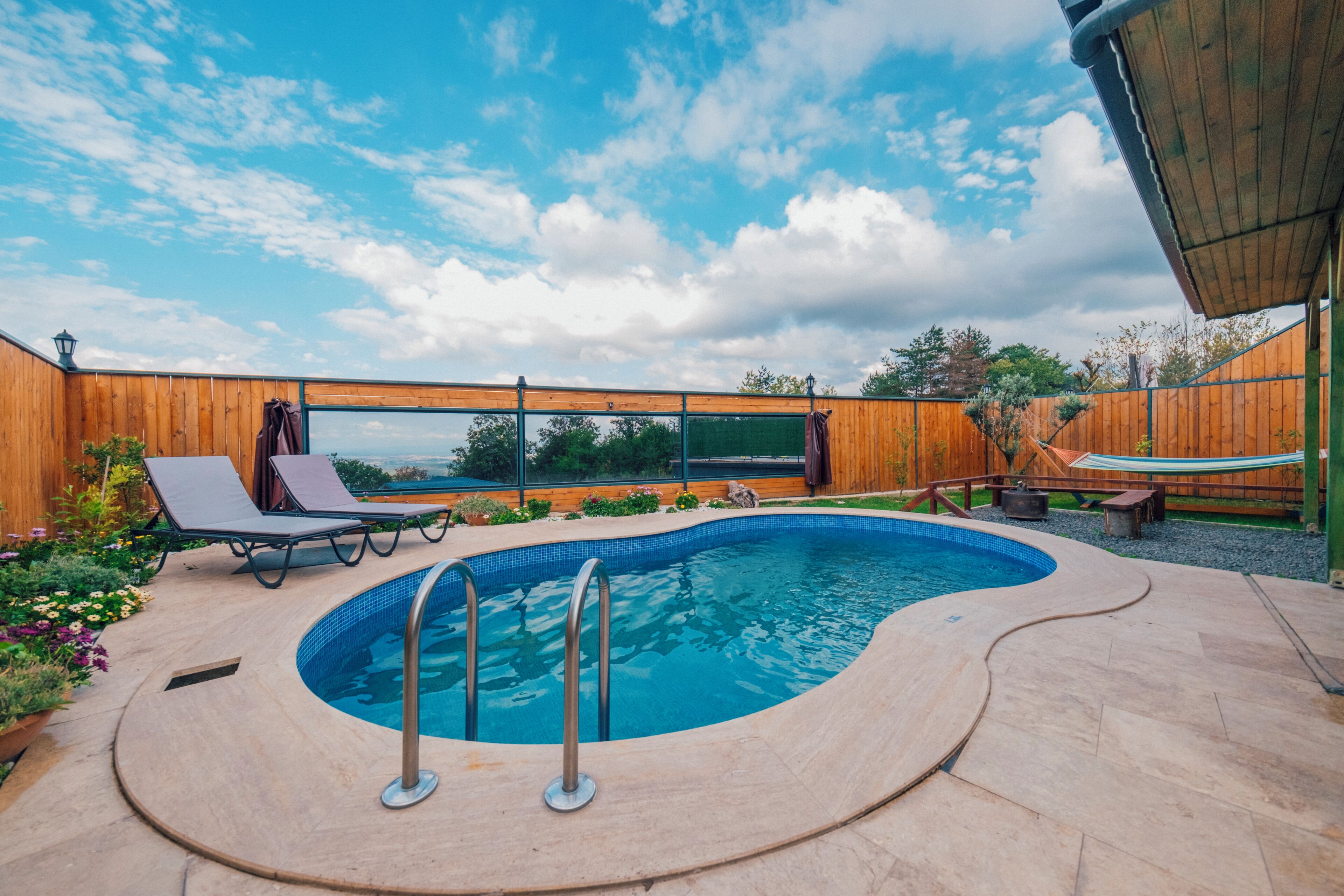 A swimming pool with a wooden deck, lounge chairs, and a view of the sky.