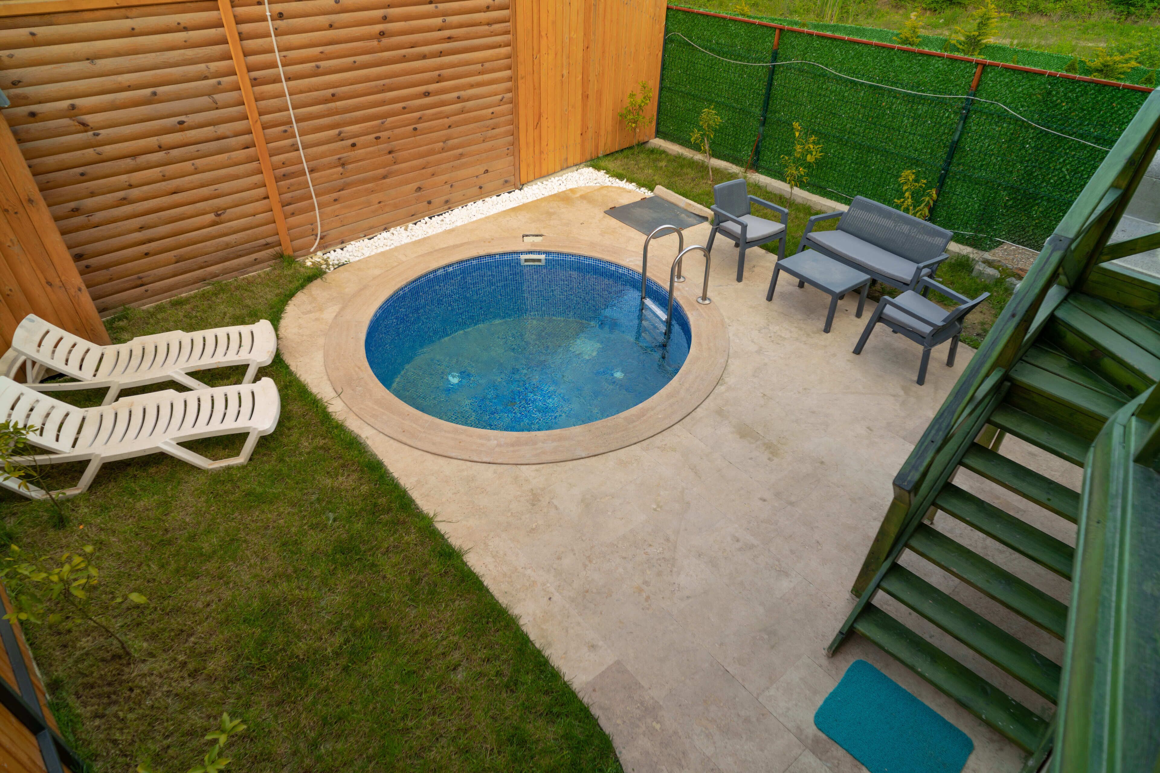 Un giardino con una vasca idromassaggio circolare, un piccolo tavolo con sedie e due poltrone da relax.